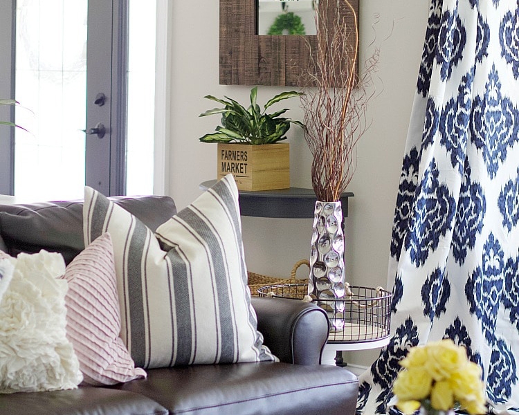 Living room with sofa and colorful pillows, with a side table, curtain, and vase. 