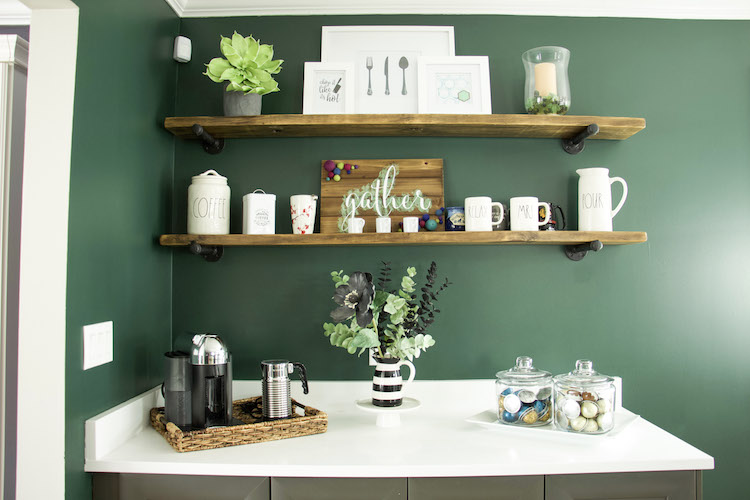 Open shelves made of dark wood against a moody dark green wall along with white countertops and grey cabinets. #ktichen #coffeestation