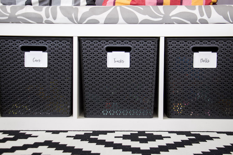 three hand lettered printable stickers labels on black bins in play room. cursive font on white bin clips.
