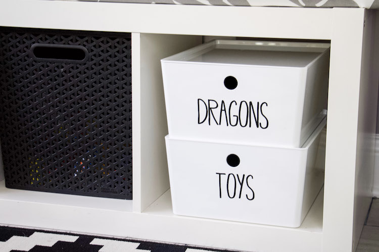 side shot of bench with white bins and black labels to demonstrate how to store action figures for toy storage