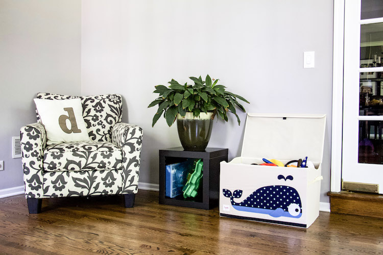 Chair with pillow next to end table with plant and toy chest with whale to hold dress-up clothing in playroom #playspace