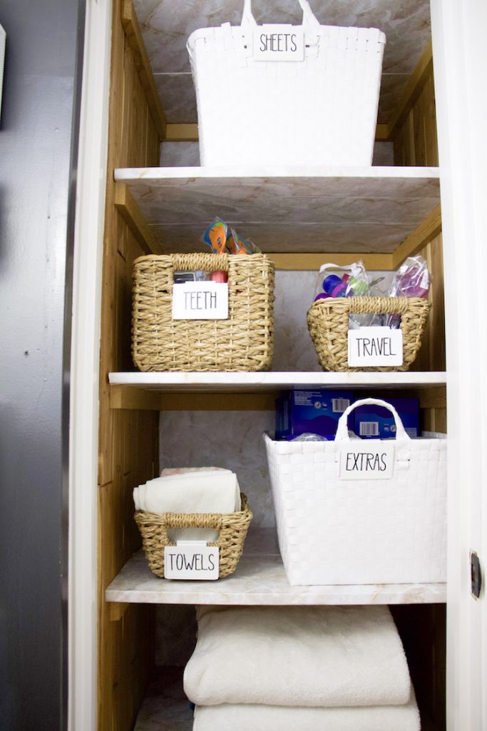 Folded towels and bins inside linen closet with marble shelf liner on shelves and back wall #linencloset
