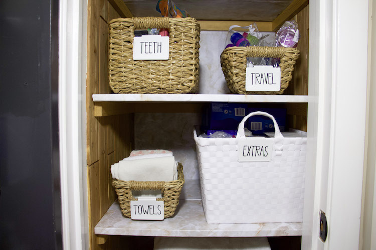 Two shelves in a linen closet with marble shelf liner and labels of extra, teeth, travel, and towels #linenclosets